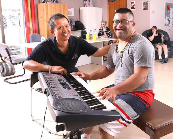 Man assisting a disabled person to play the piano