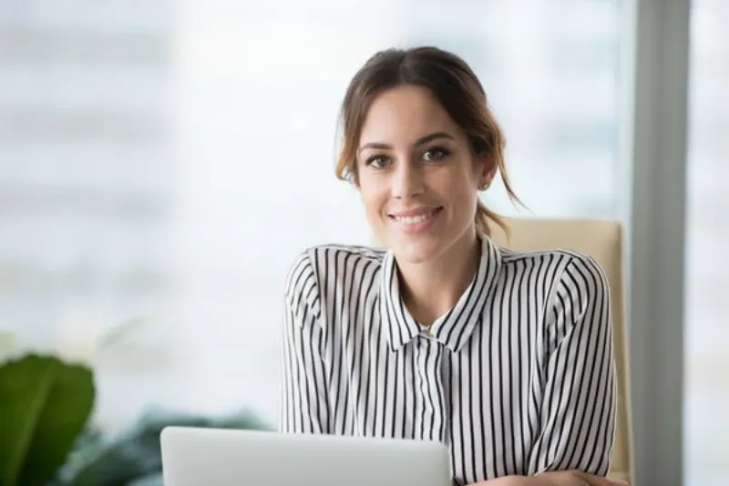 Woman smiling while working on a laptop in an office setting